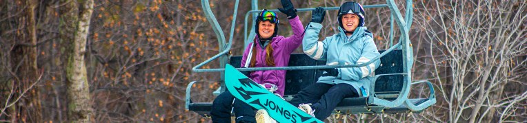 Two people on ski lift with snowboard and ski